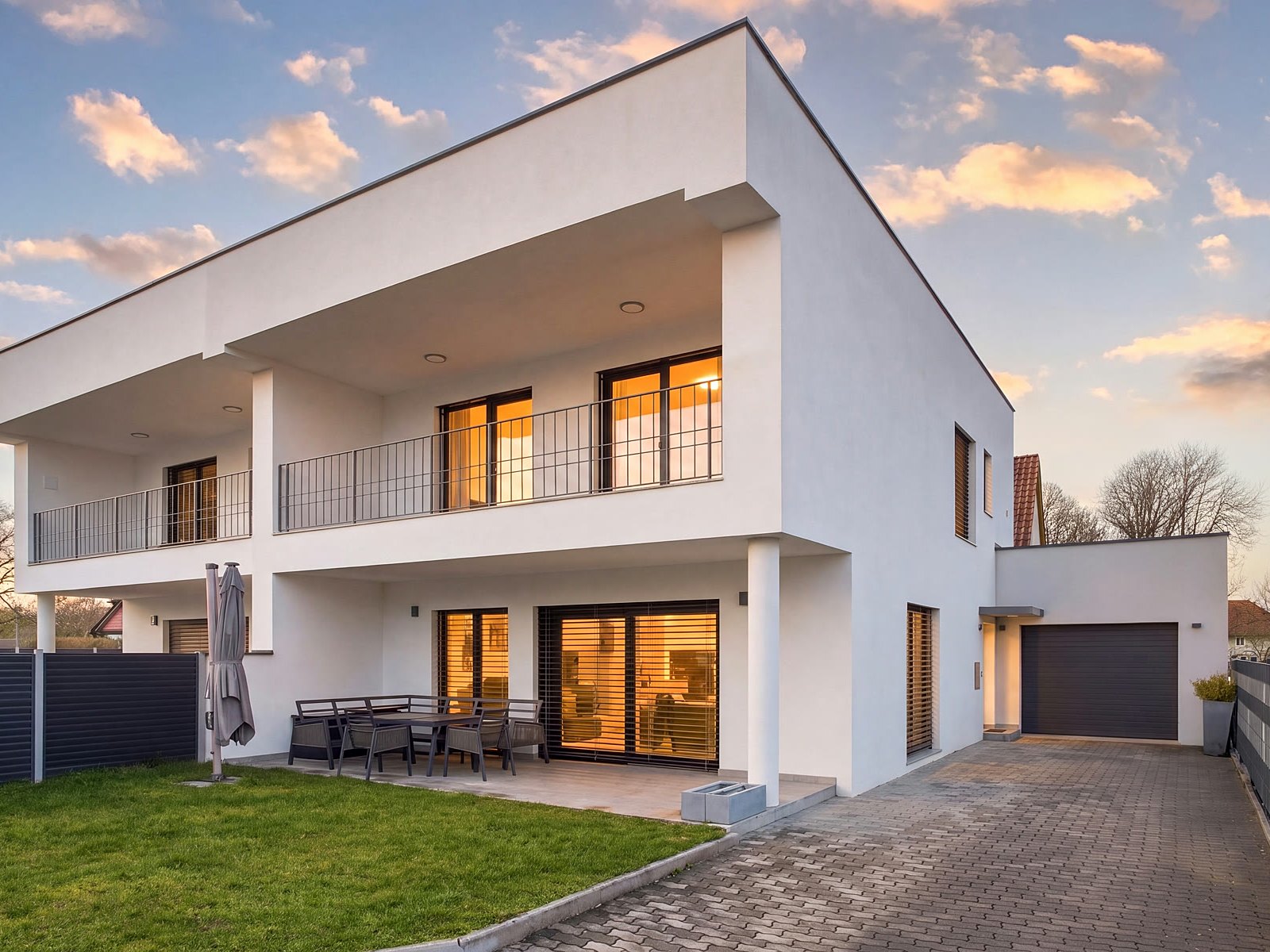 Modernes Einfamilienhaus in der Dämmerung, warm beleuchtete Fenster vor rosa Abendhimmel