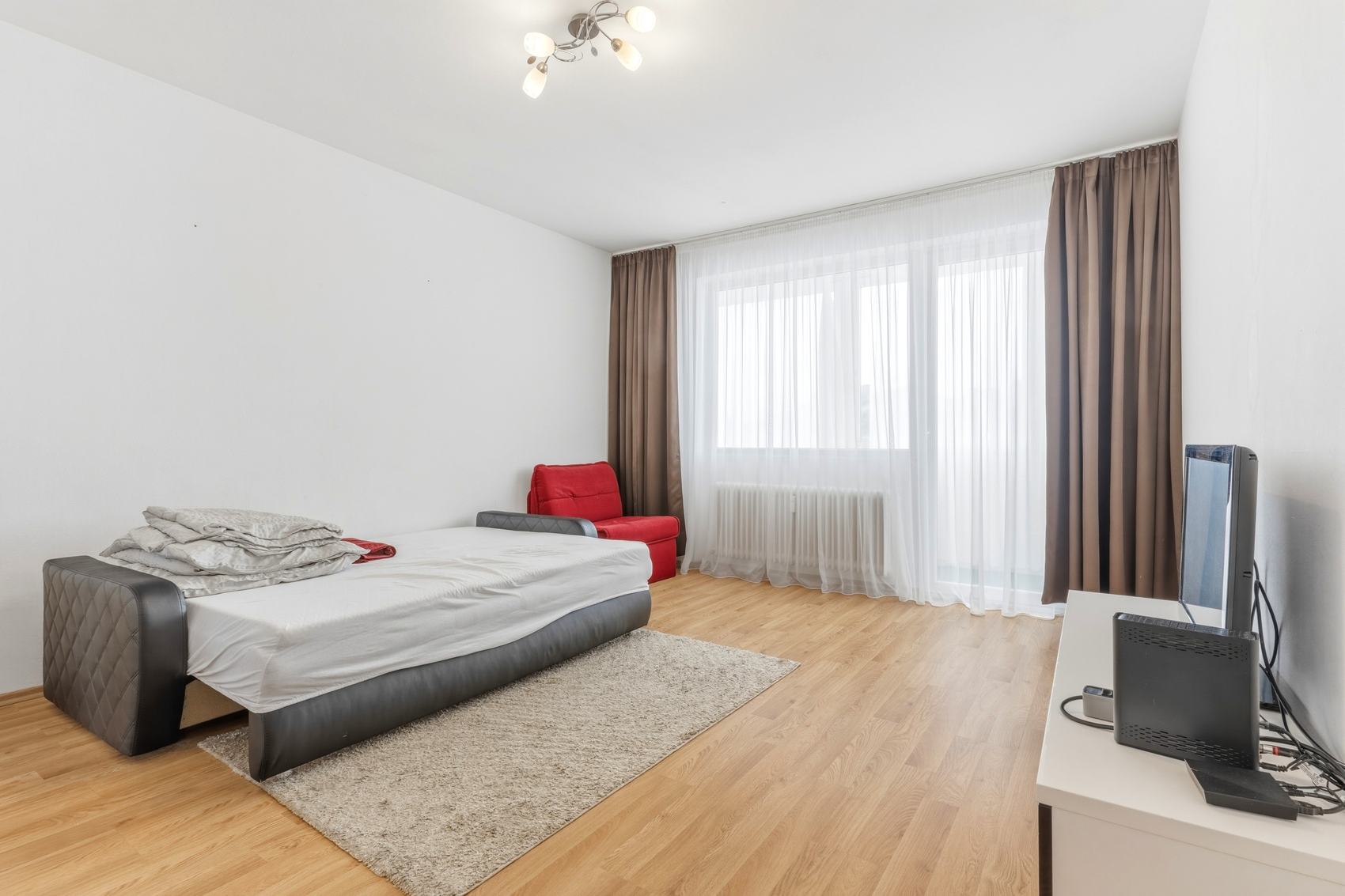 Wohnzimmer mit Bett, rotem Sessel und Balkontür