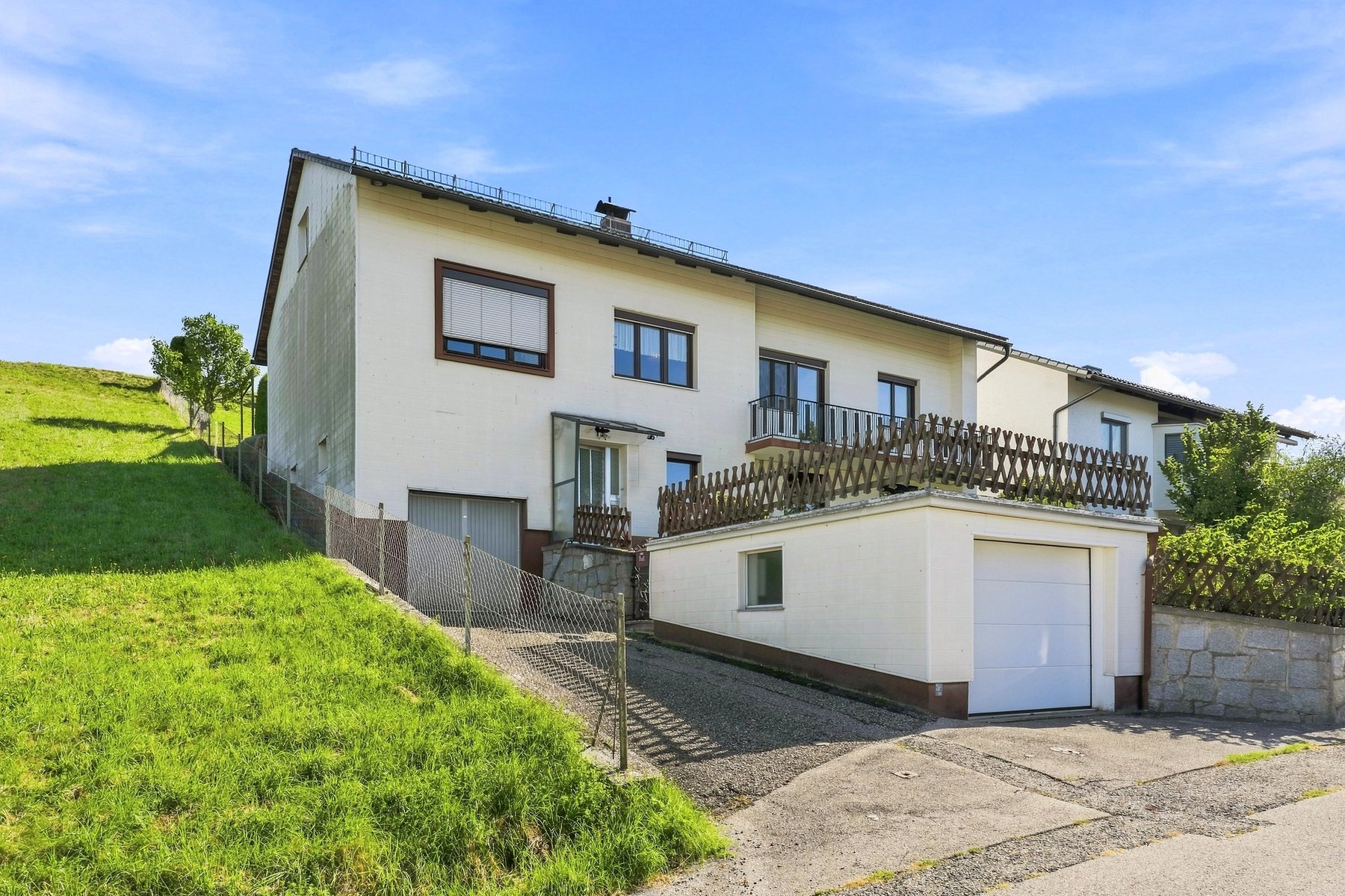 Weißes Einfamilienhaus mit Balkon auf einer Wiese unter blauem Himmel